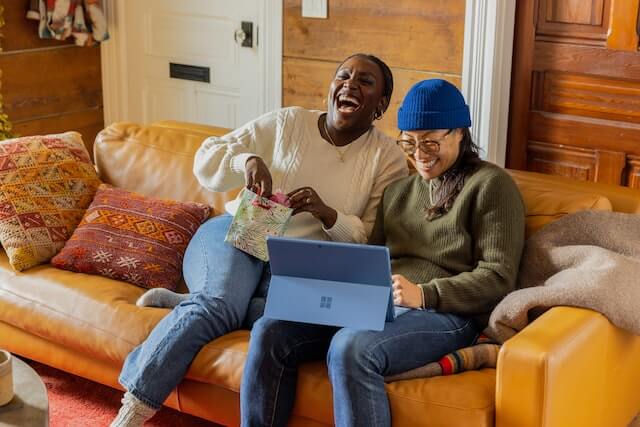 ソファーに座ってパソコンを見ながら笑っている二人の女性